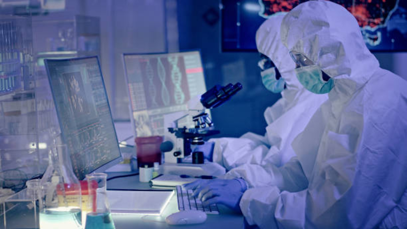 Young multi-ethnic team during coronavirus lab tests. Working on computers. Map of disease outbreaks in background